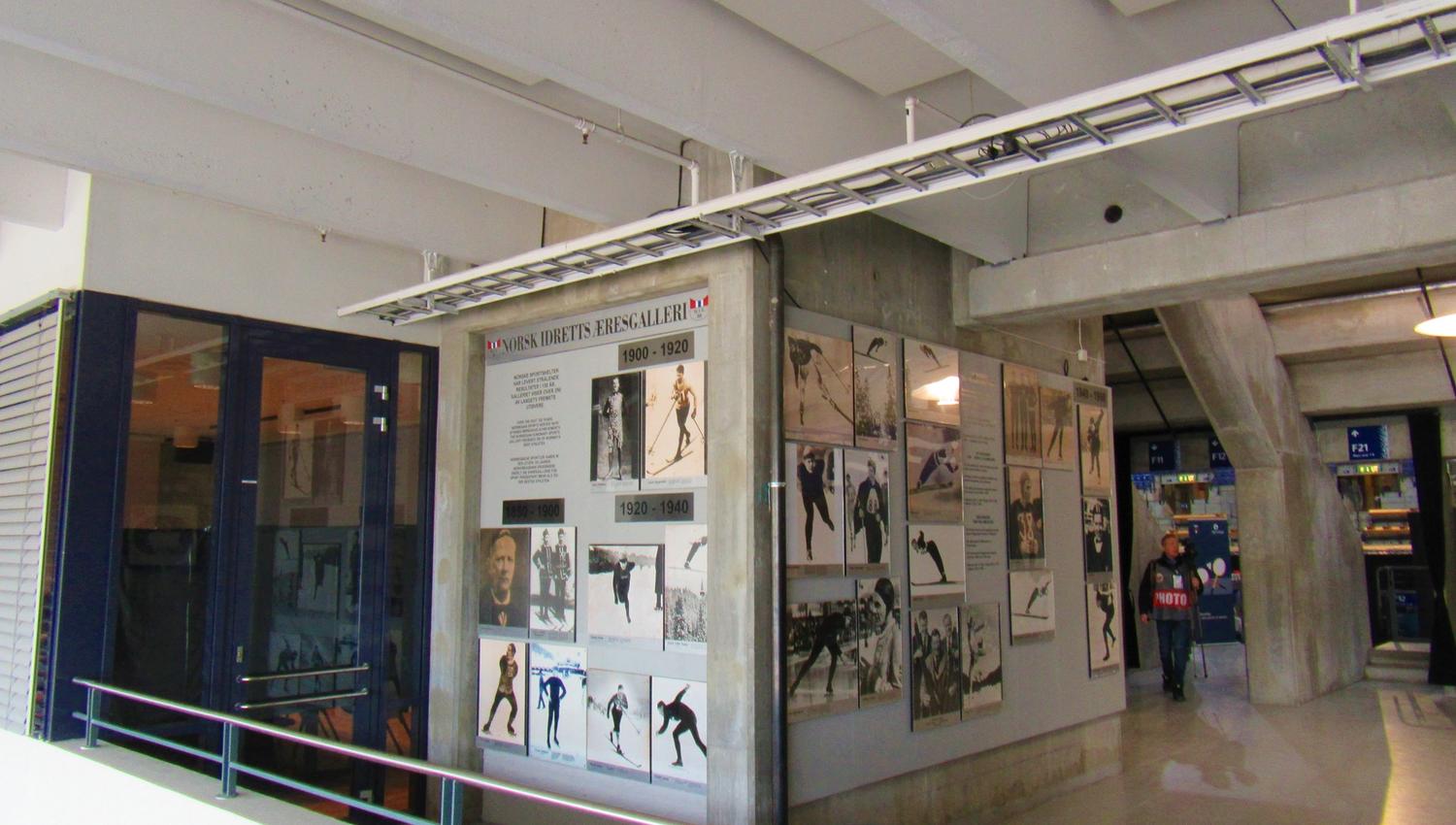 Innendørs gang med betongtak og utstillingsvegger med historiske foto og tekstplakater, samt en person i bakgrunnen..
