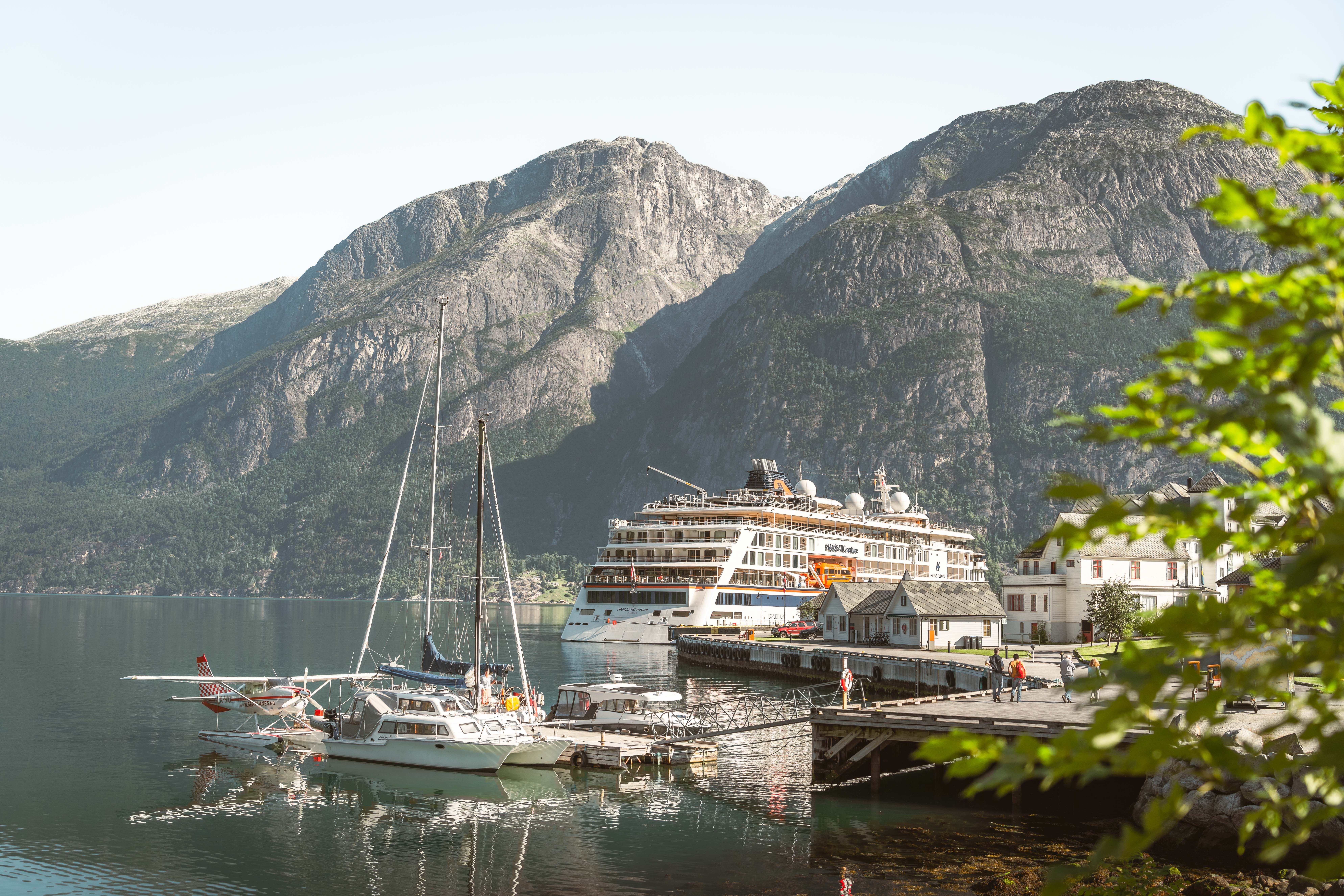 The harbour area with a cruise ship, a couple of sail boats, a seaplane and people on the dock.