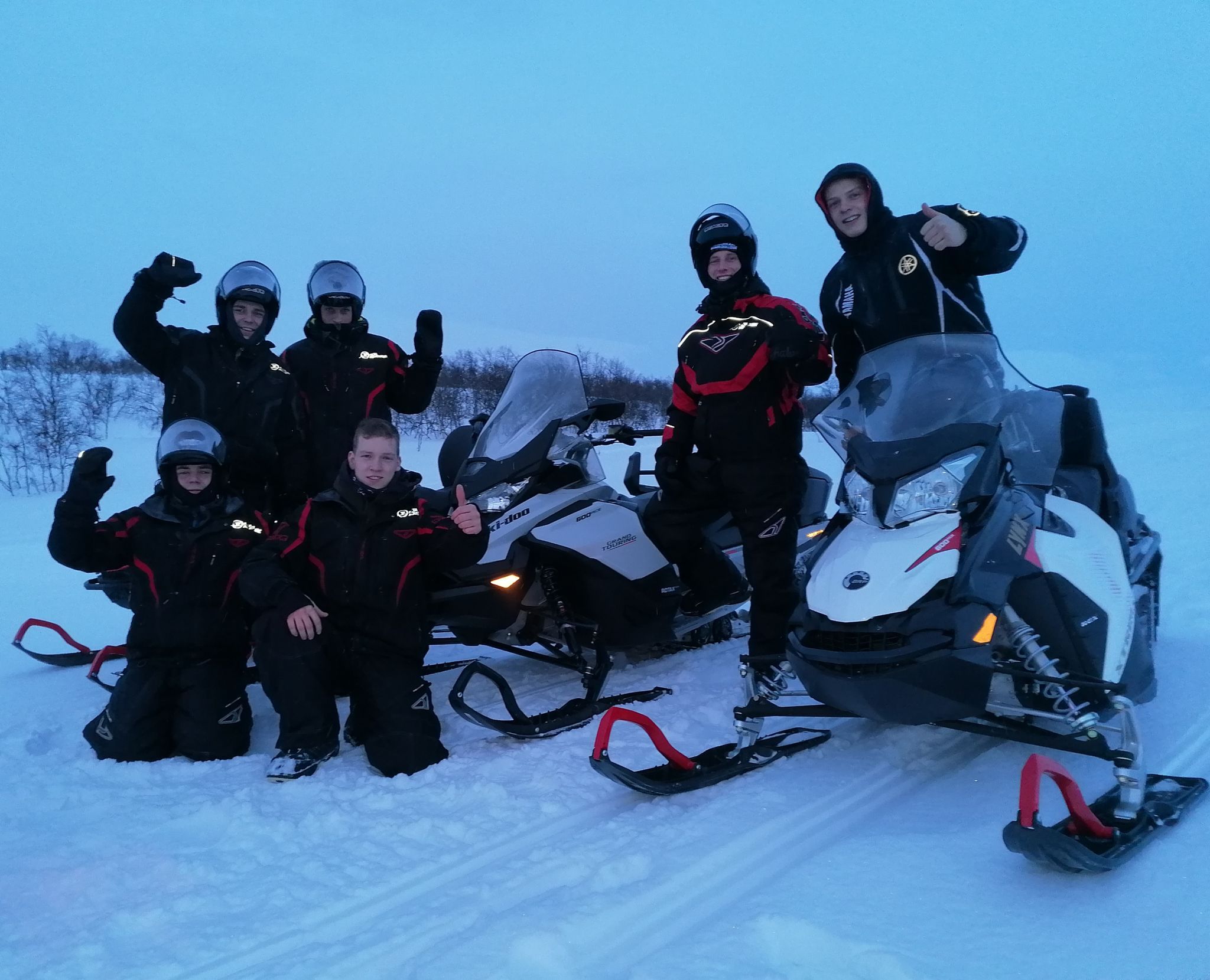 Groupe de jeunes souriants en tenue de motoneige dans la neige.