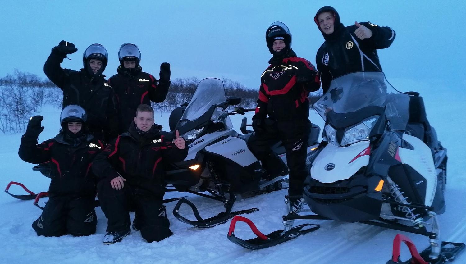 Groupe de jeunes souriants en tenue de motoneige dans la neige.