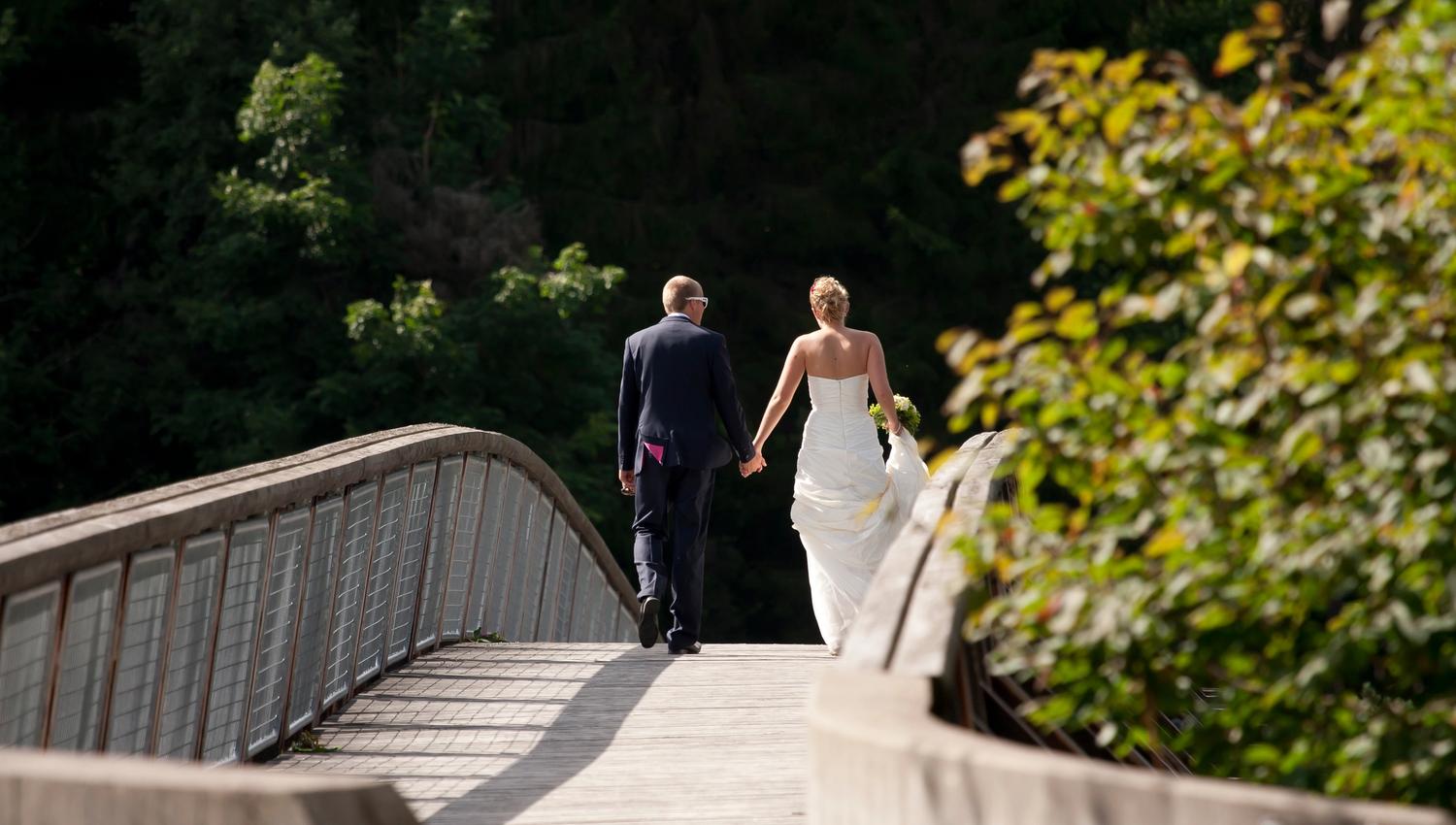 Bride and groom walk across the bridge in Kjærra Fossepark