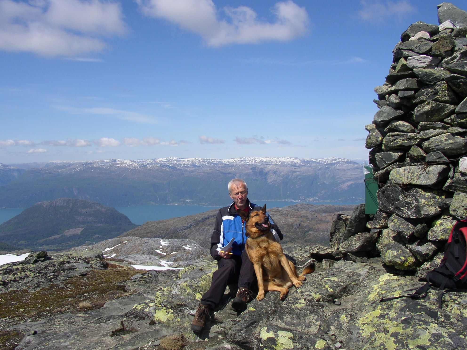 a man and a dog posing at the top by the cairn 