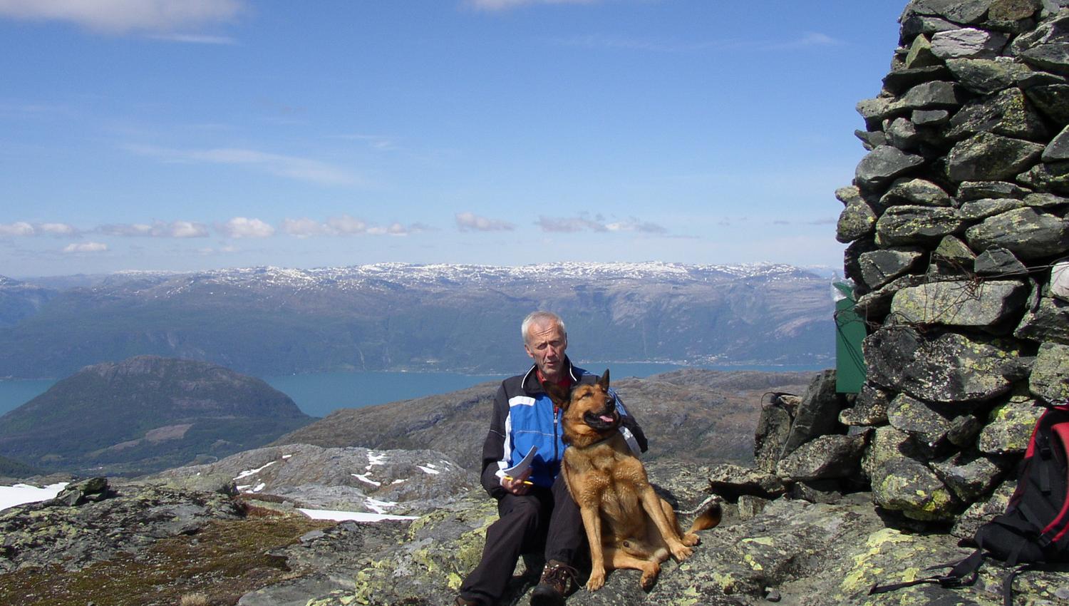 a man and a dog posing at the top by the cairn