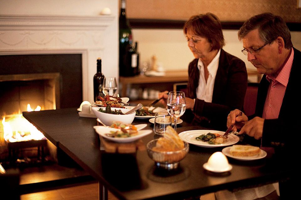 A man and a woman eating dinner next to a fireplace.