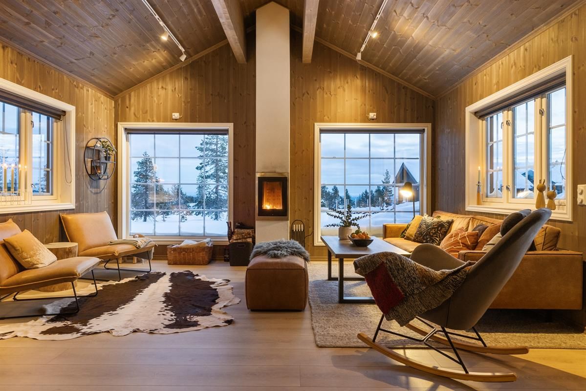 A bright, modern living room with large windows, a view of snowy nature, and a fireplace.