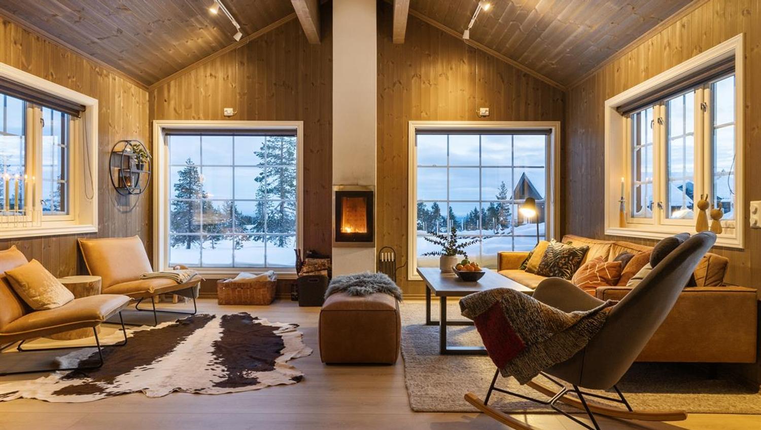 A bright, modern living room with large windows, a view of snowy nature, and a fireplace.