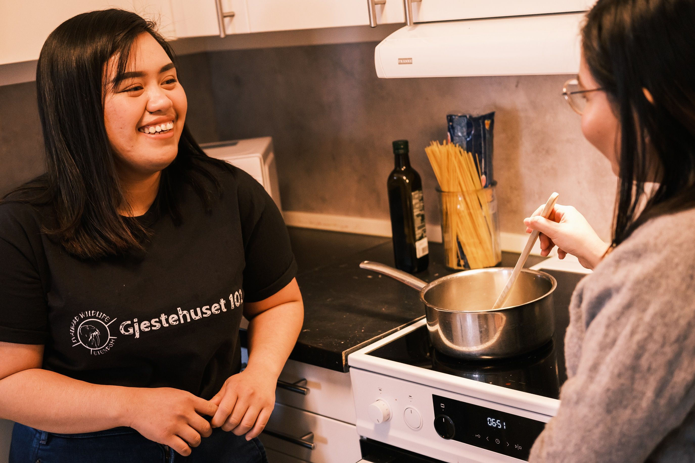 Two persons looking at each other while cooking a meal on a stove.