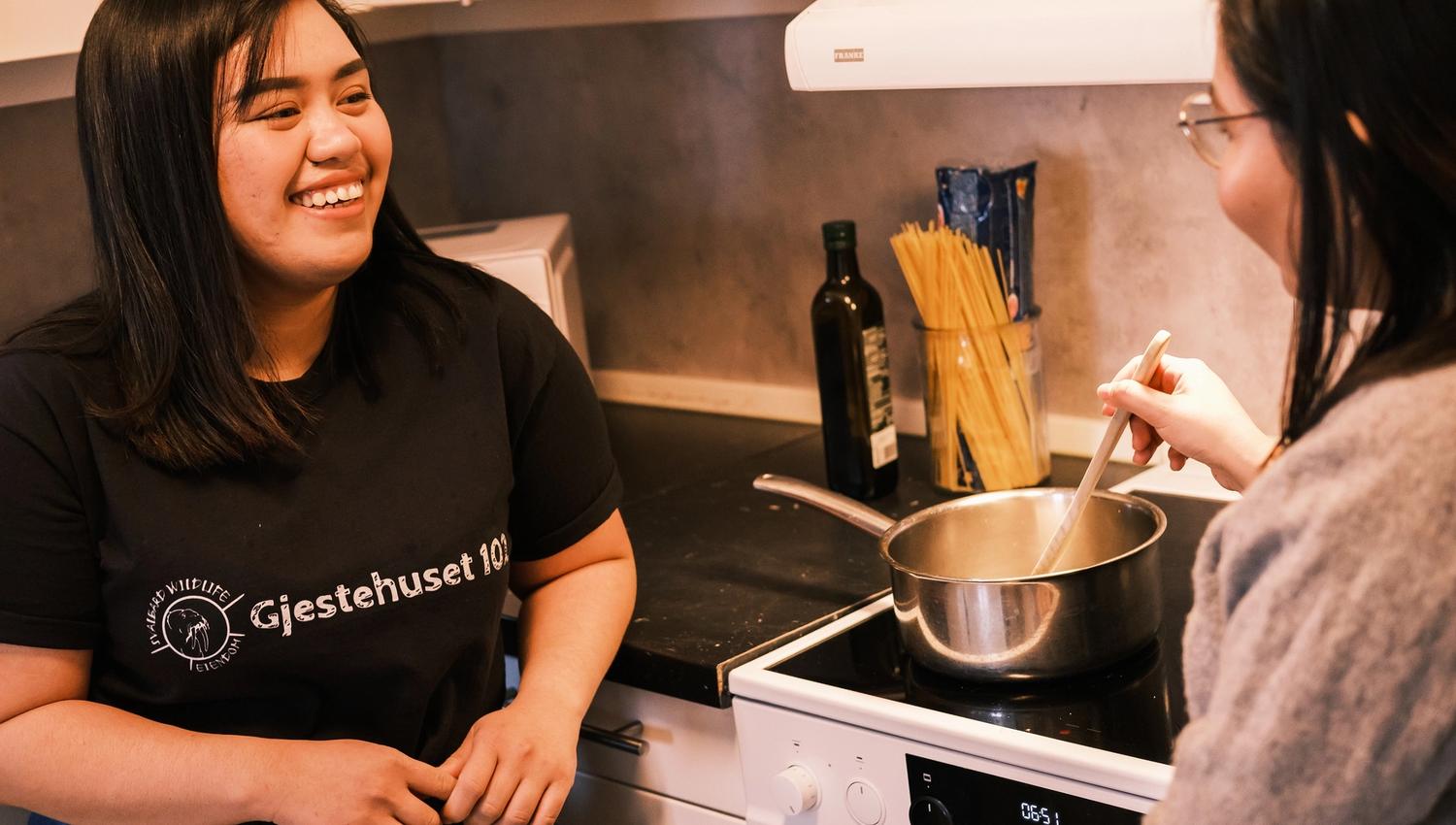 Two persons looking at each other while cooking a meal on a stove.