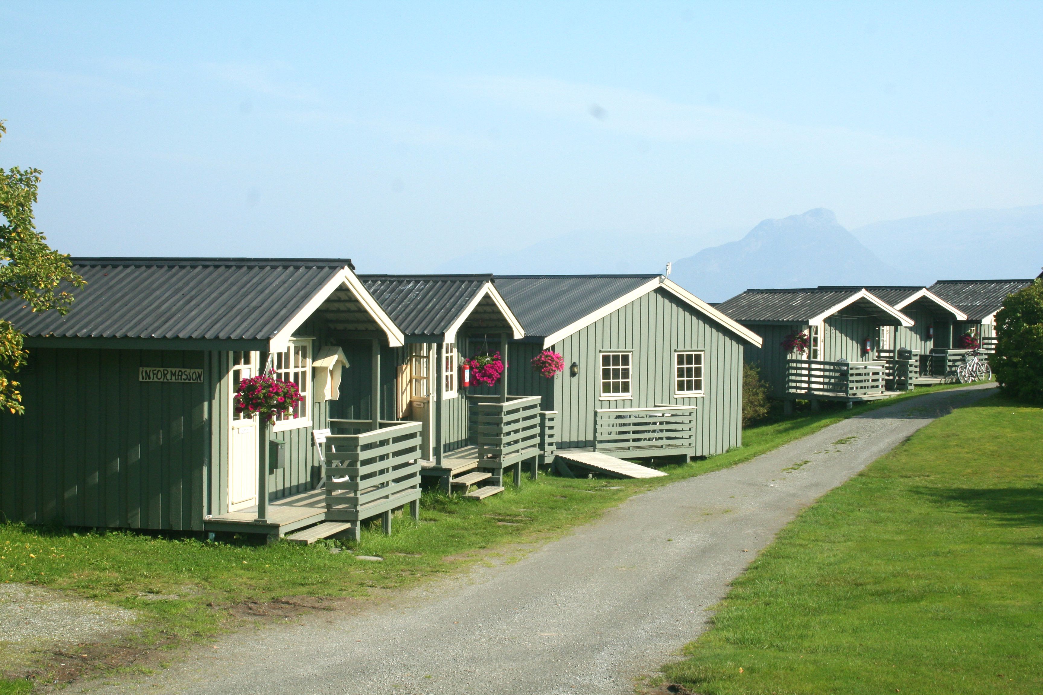 Information cabin and lined cottages at Oddland Camping, surrounded by green lawns and summer flowers.