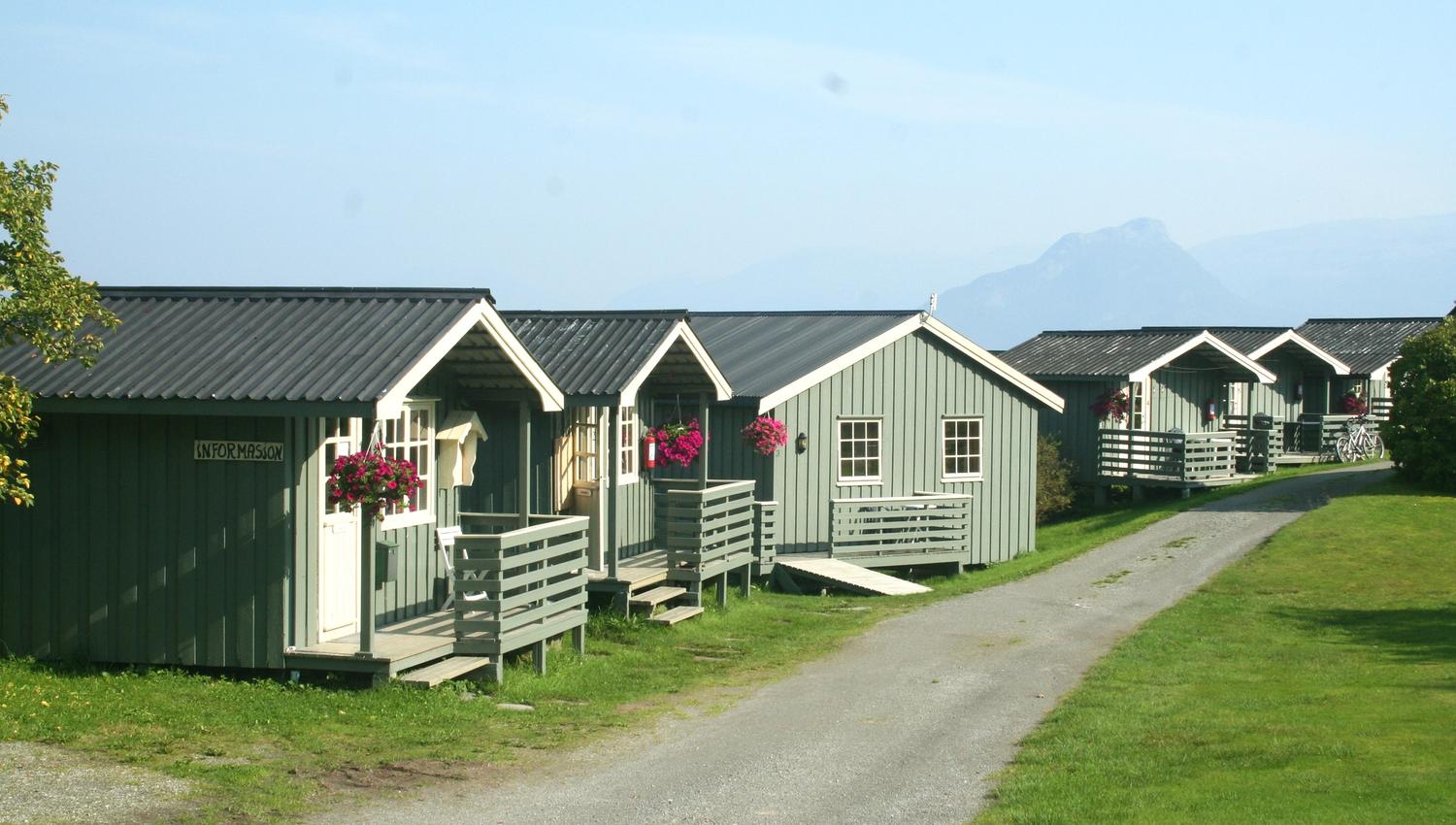 Information cabin and lined cottages at Oddland Camping, surrounded by green lawns and summer flowers.