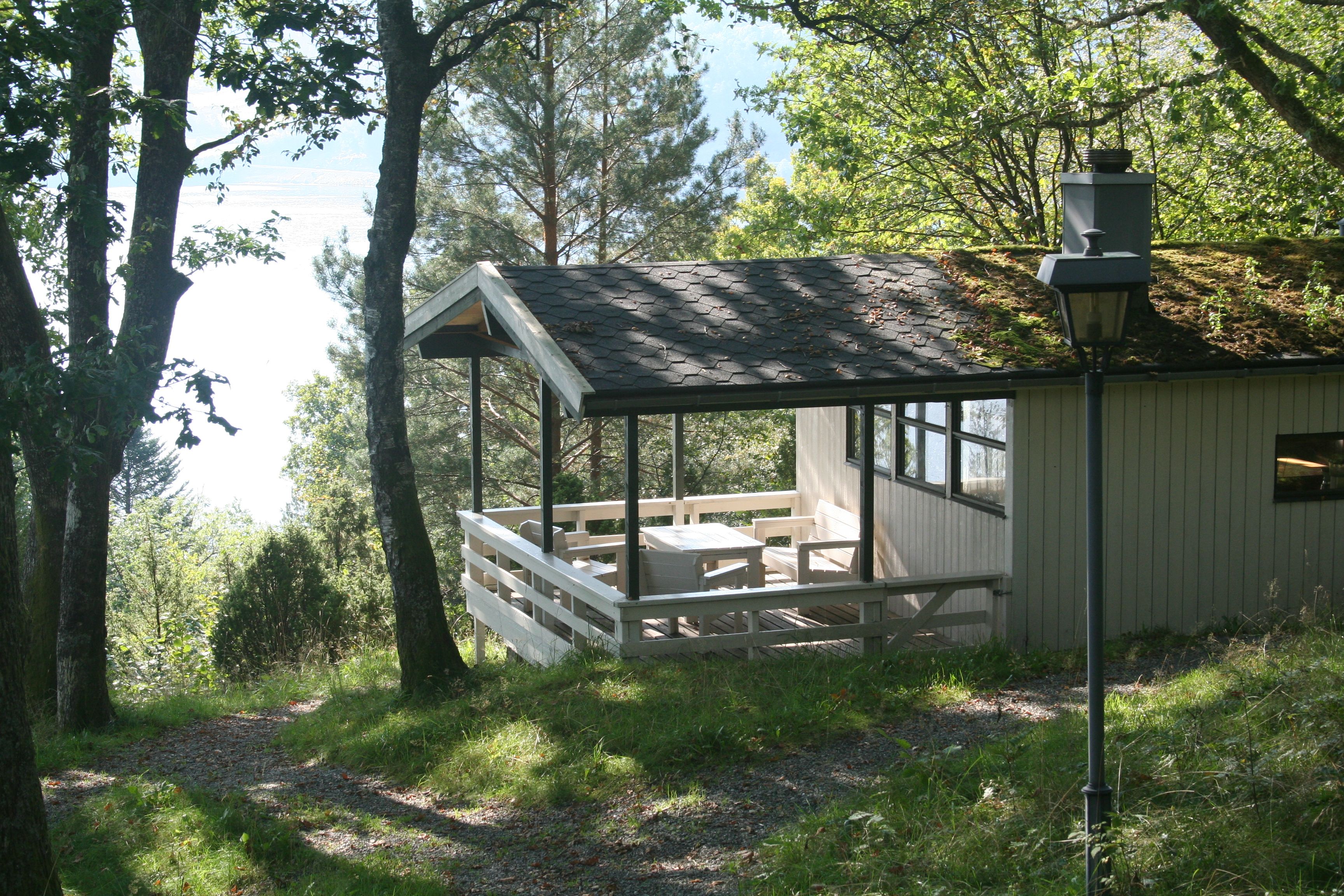 Cabin with terrace surrounded by forest and fjord views.