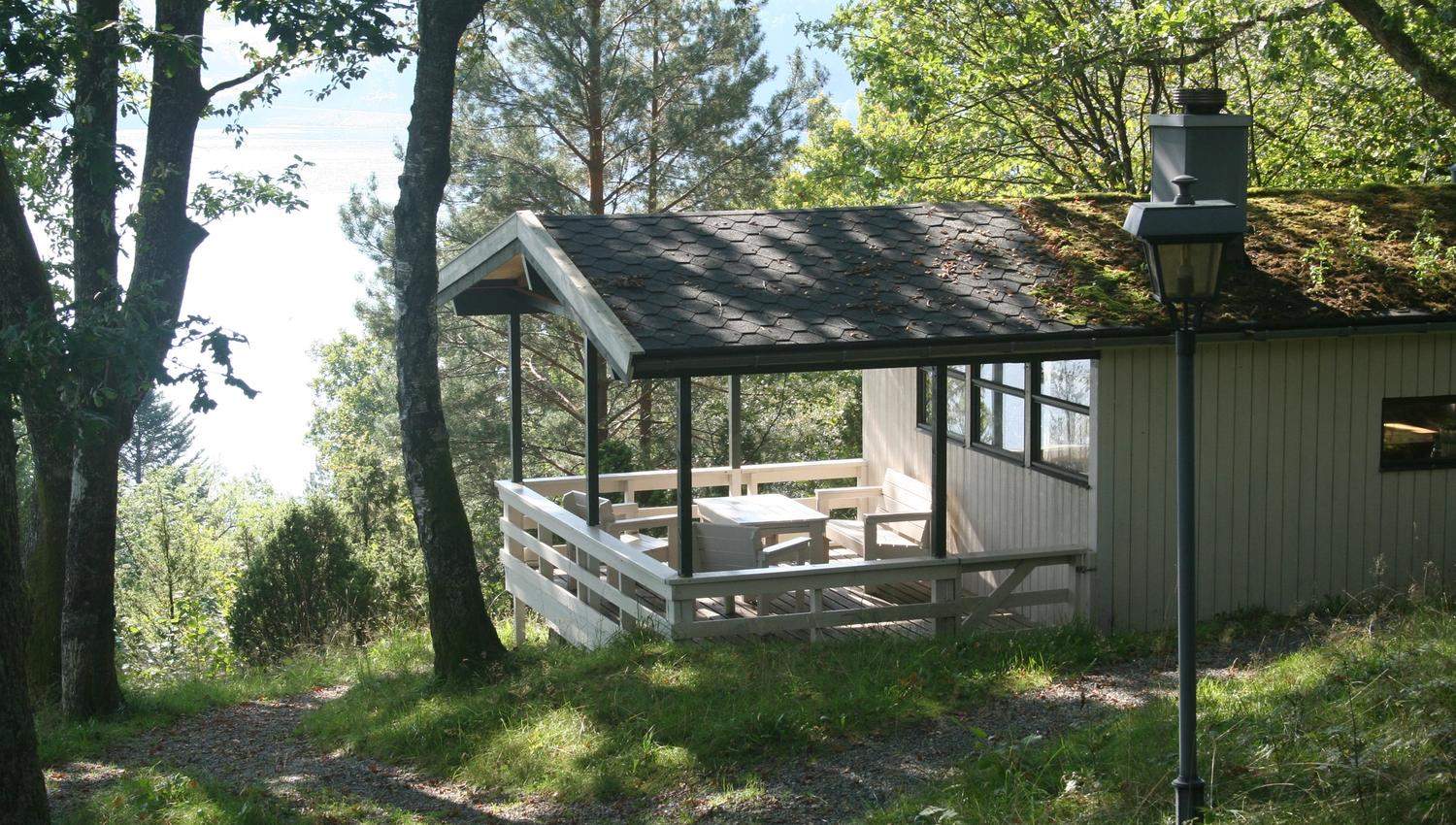 Cabin with terrace surrounded by forest and fjord views.