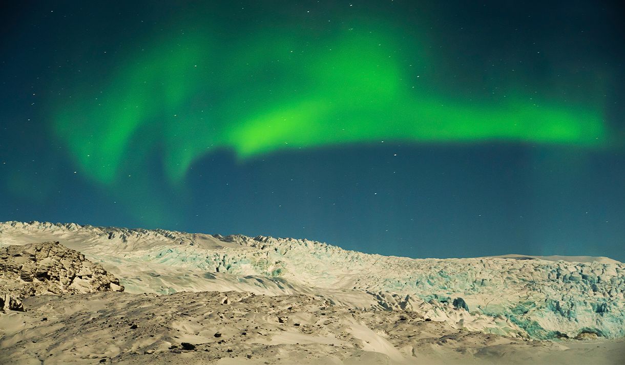 Northern lights under a dark sky above a large glacier