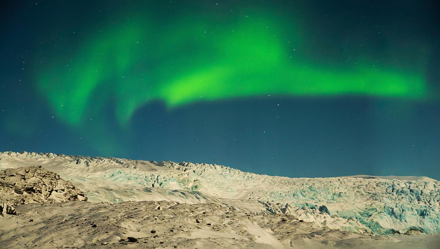Northern lights under a dark sky above a large glacier