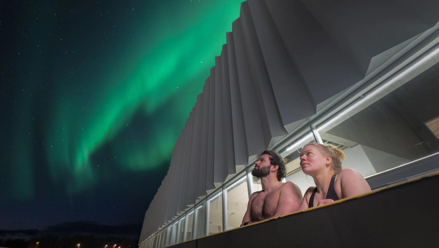 A man and a woman enjoying the Northern Lights from the pool