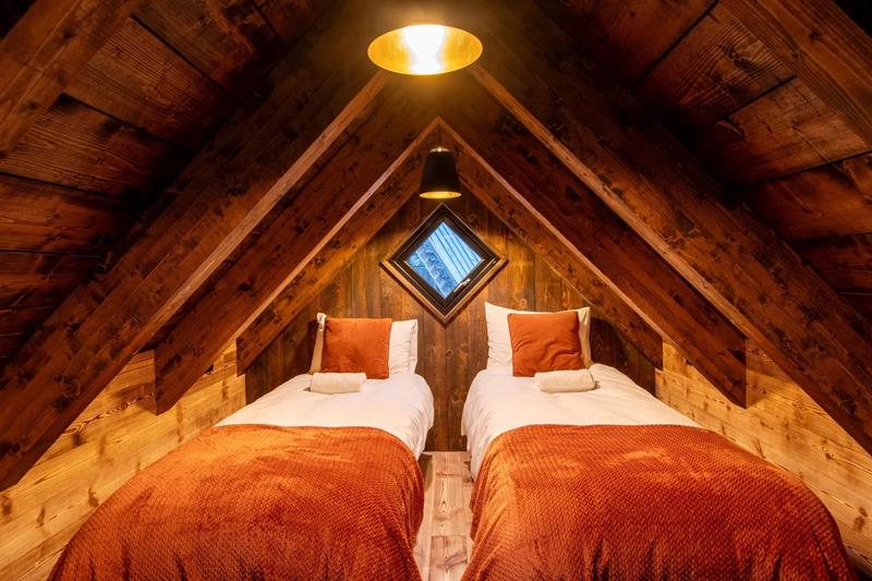 Soverom på hemsen i vikinghytte på Lothepus Camping med to senger under takmønet og varme orange tekstilar
