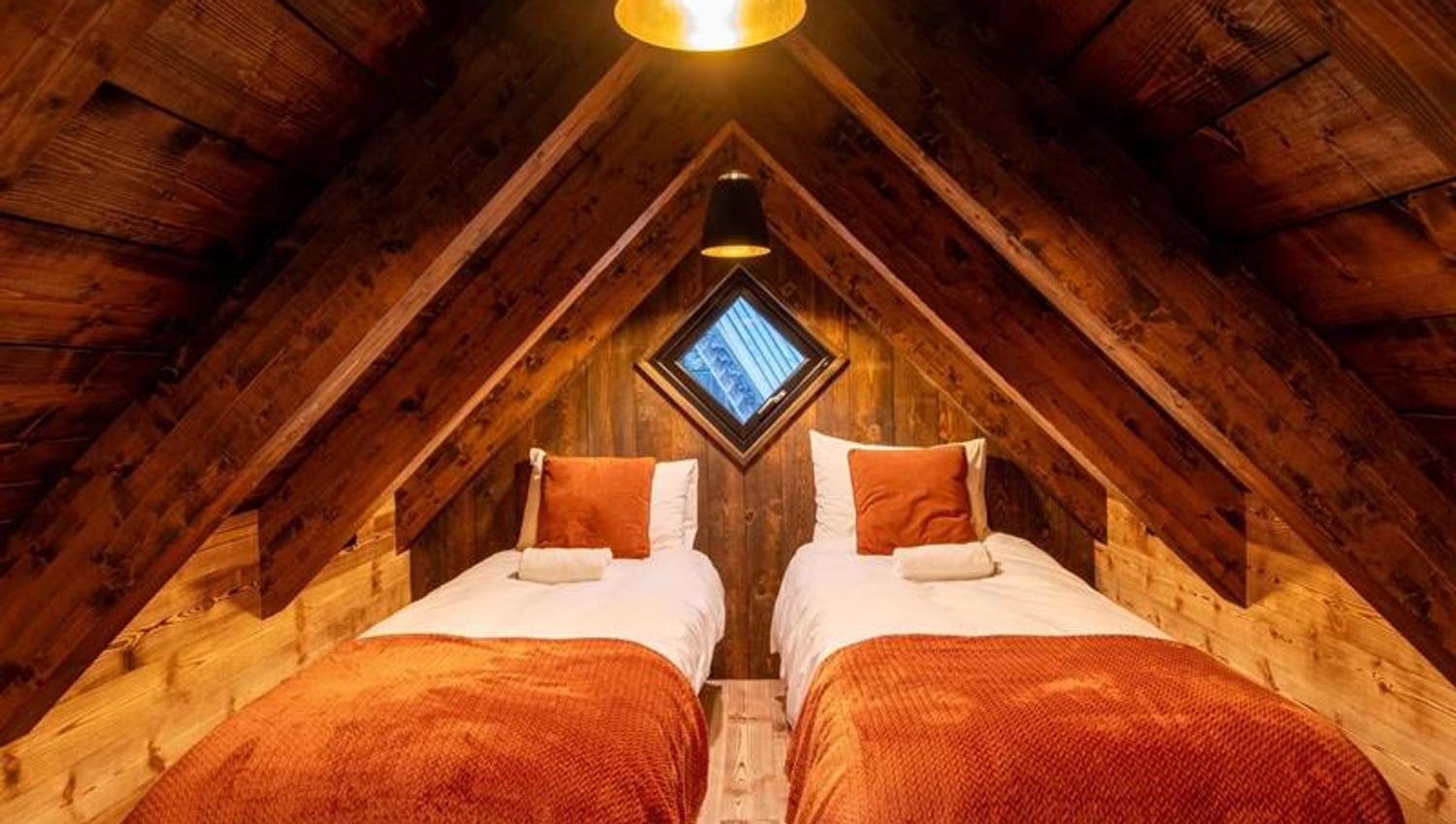 Soverom på hemsen i vikinghytte på Lothepus Camping med to senger under takmønet og varme orange tekstilar