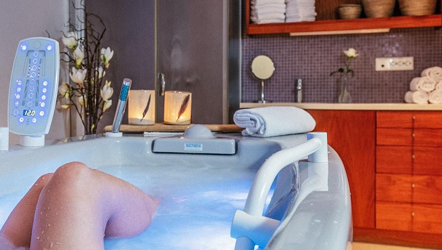 Person soaking in a bubbling jacuzzi tub in a spa-like bathroom with towels, candles, shelves, and a shower stall at Hotel Alexandra..