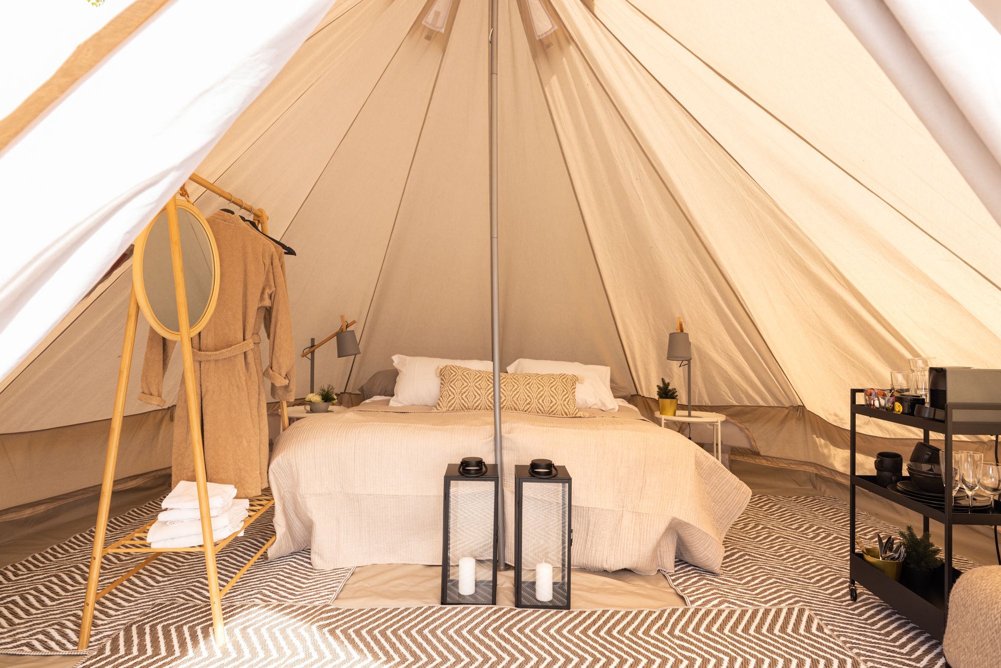 View of the inside of the tent with doublebed, wardrobe rack, table and decorating details. 