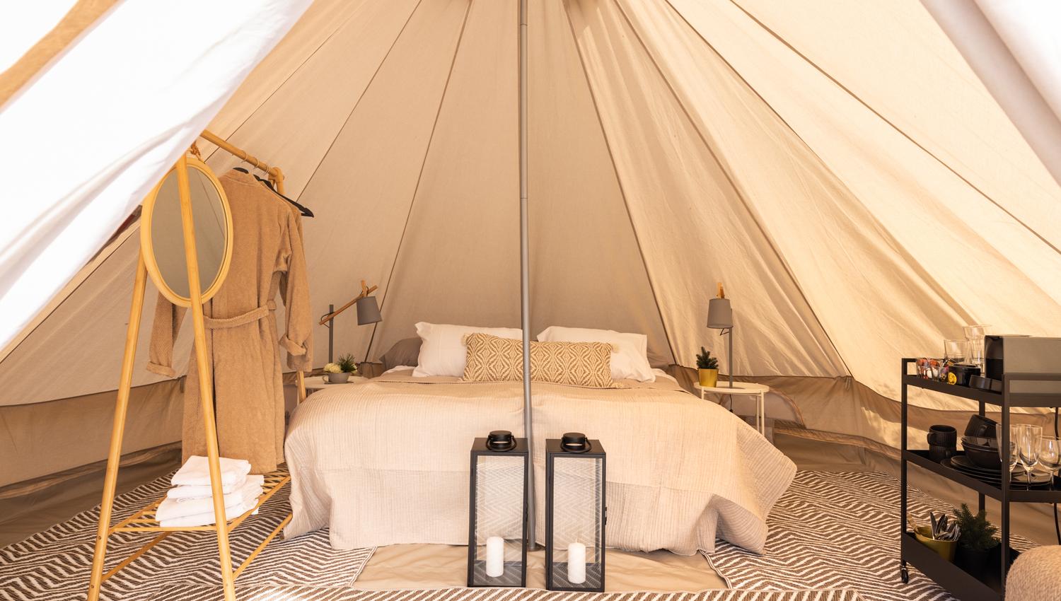 View of the inside of the tent with doublebed, wardrobe rack, table and decorating details.