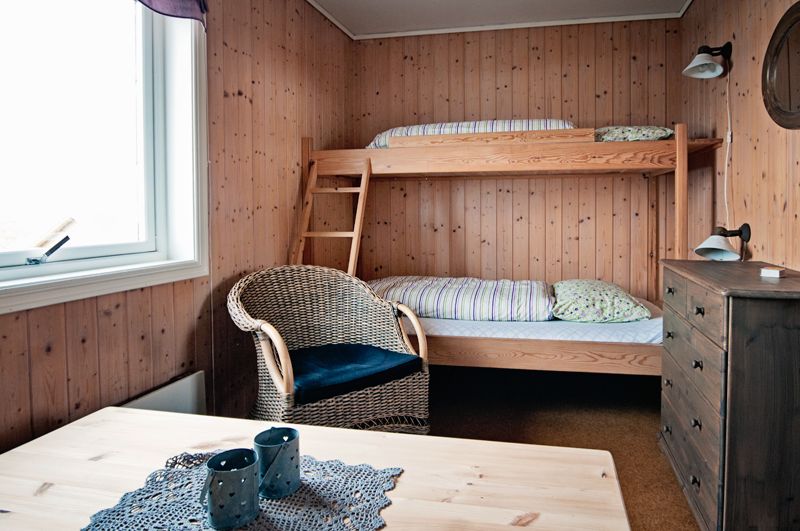 A room with wooden walls, a bunk bed, dresser, chair and table.