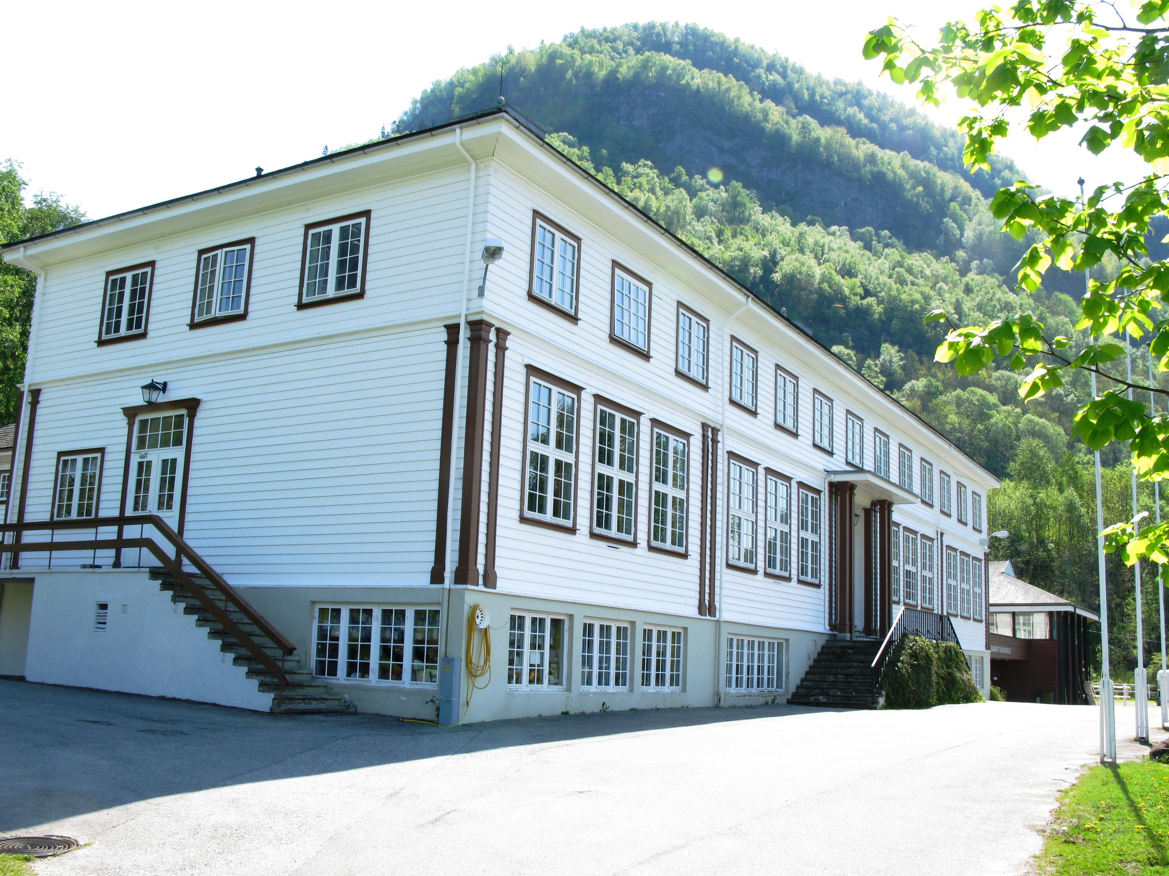 Close-up view of Hardanger Hostel B&B – a traditional wooden house with green forested mountains behind.
