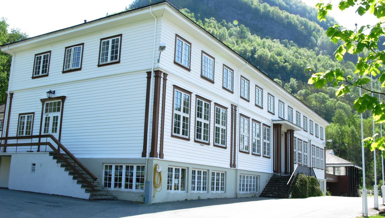 Close-up view of Hardanger Hostel B&B – a traditional wooden house with green forested mountains behind.