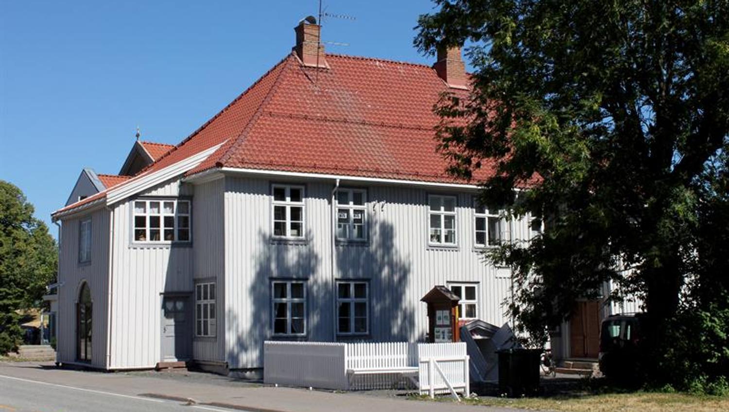 Image of the museum from the outside. A beautiful light gray painted wooden house with red roof tiles and white picket fence