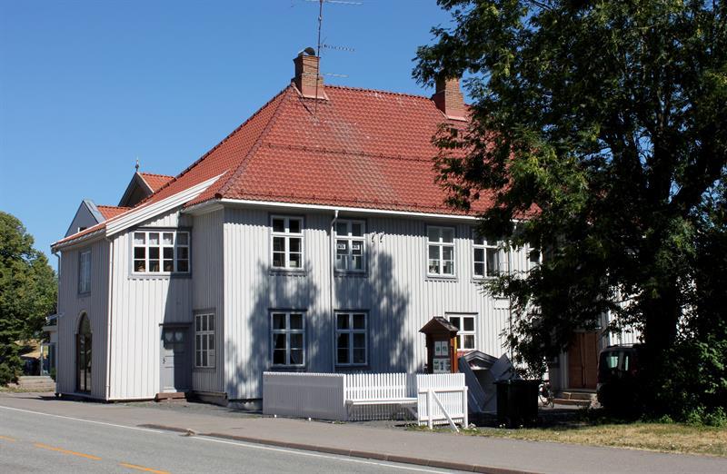 Image of the museum from the outside. A beautiful light gray painted wooden house with red roof tiles and white picket fence