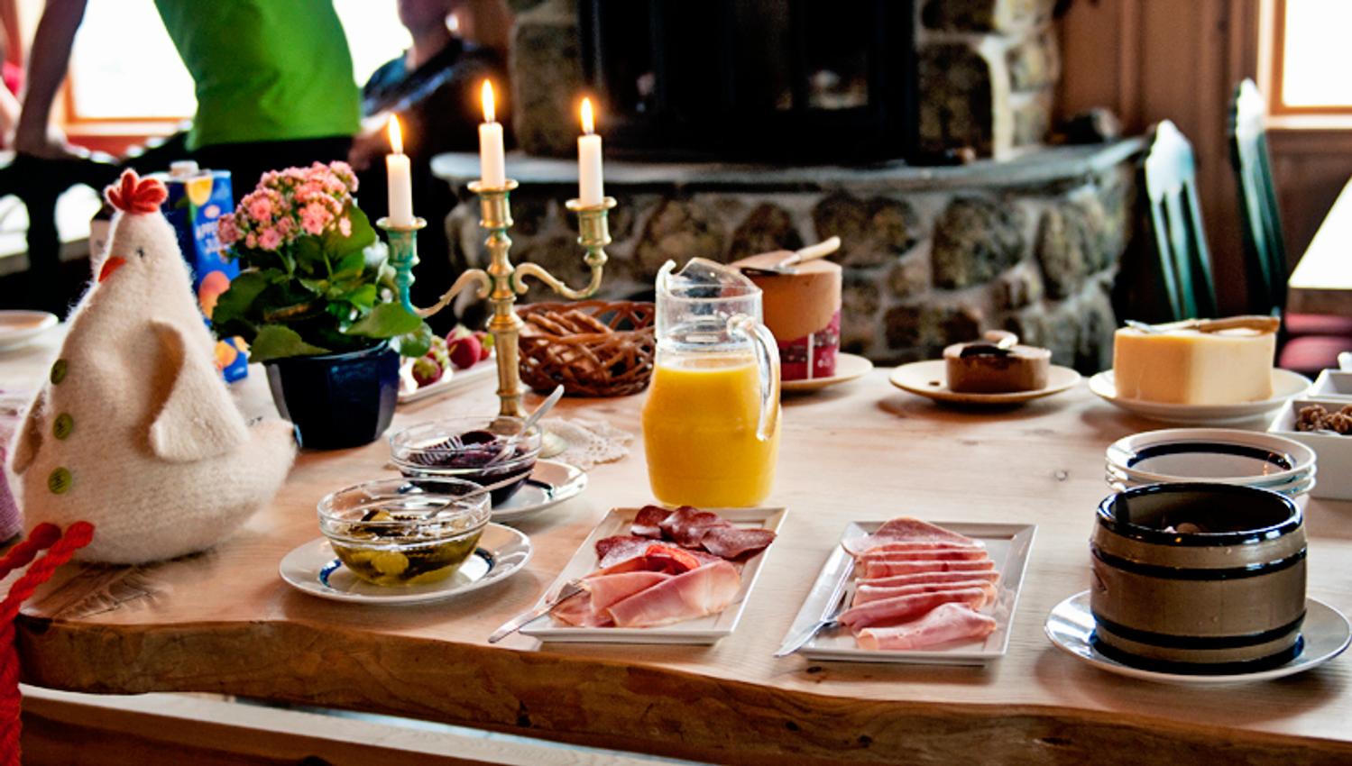 Breakfast table with candles, an easter chicken, orange juice and different bread spreads.