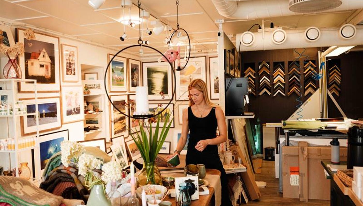 Inside the gallery at Iversen Bakery and Gallery, a woman works with ceramics and interior items surrounded by artworks, frames and handmade products.