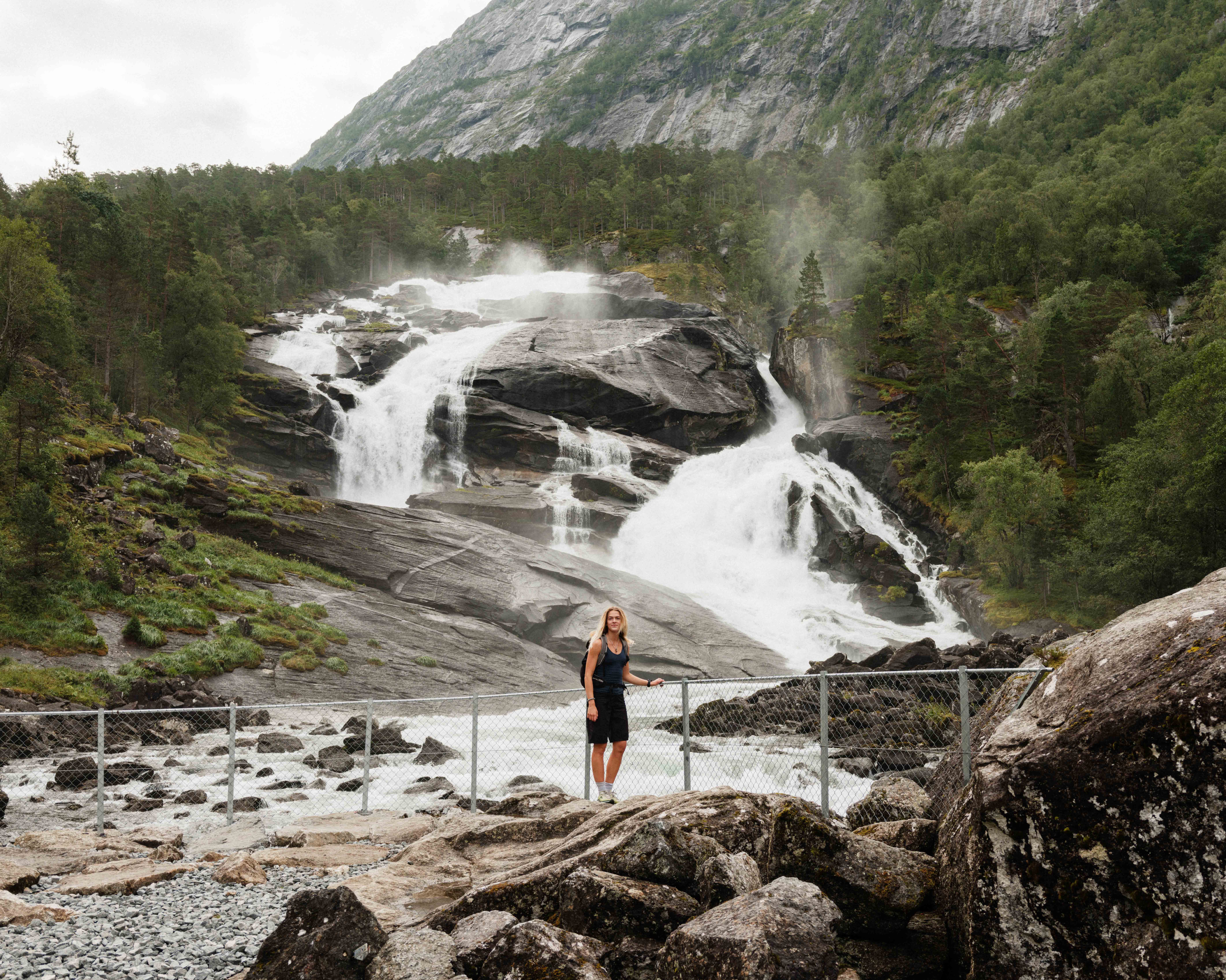 Woman by the riverbank below Tveitafossen – the first waterfall along the Husedalen hike.