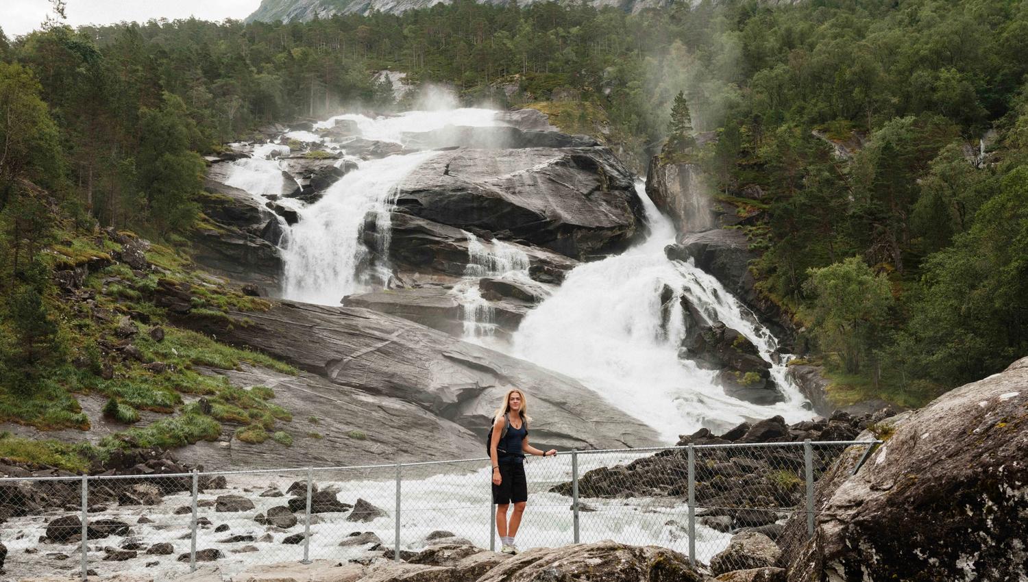Woman by the riverbank below Tveitafossen – the first waterfall along the Husedalen hike.