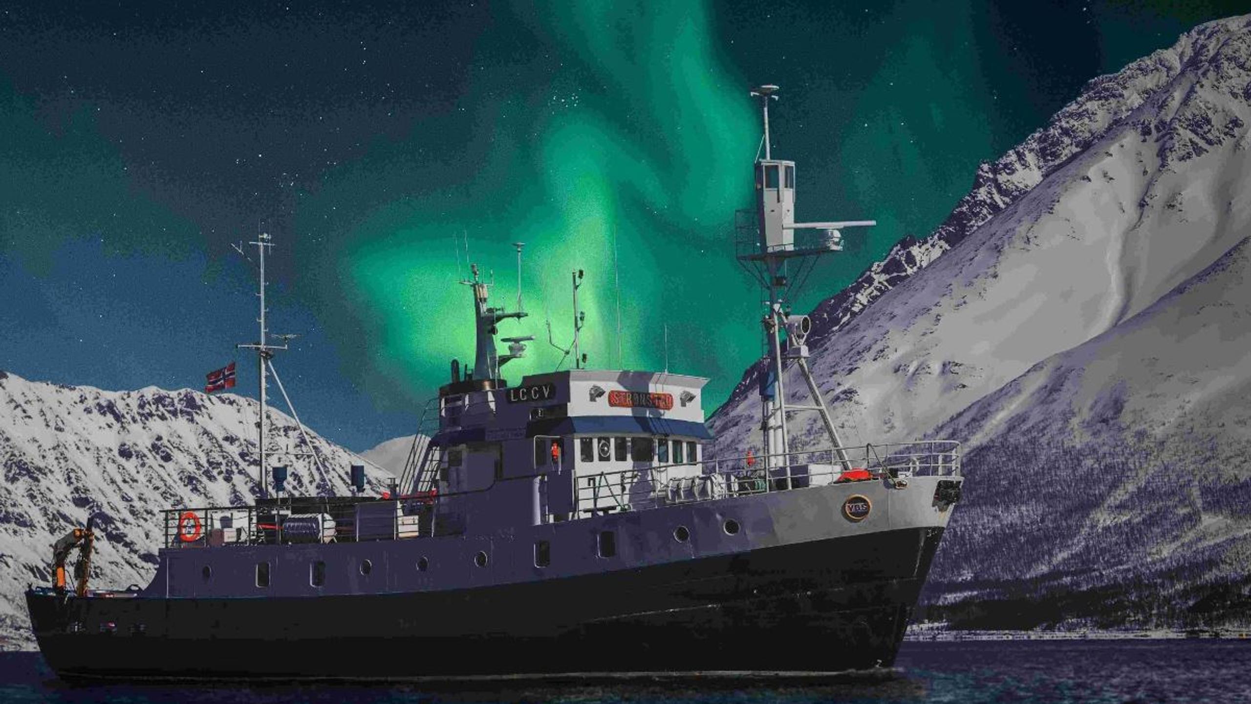 MS Strønstad på fjorden under nordlyset, omgitt av snødekte fjell nær Tromsø.