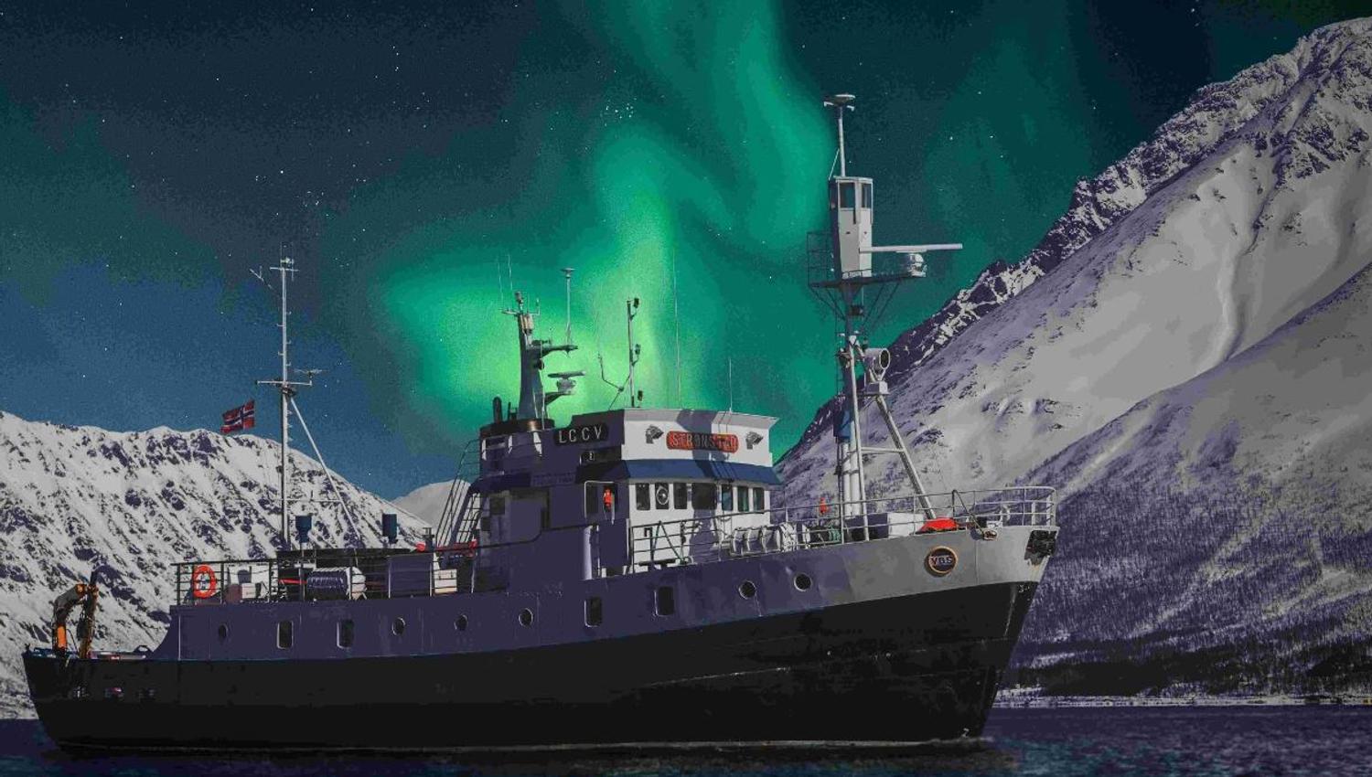MS Strønstad på fjorden under nordlyset, omgitt av snødekte fjell nær Tromsø.