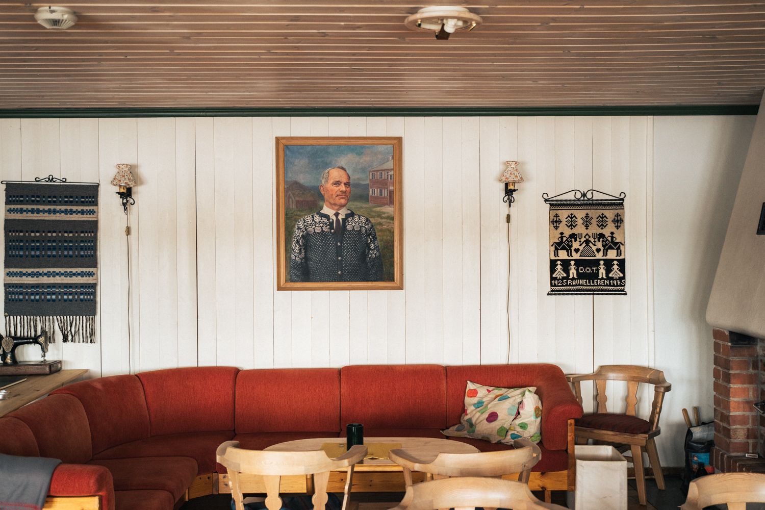 Inside the lodge, a lounge area with a red couch, wooden sitting chairs and a painting on the wall.