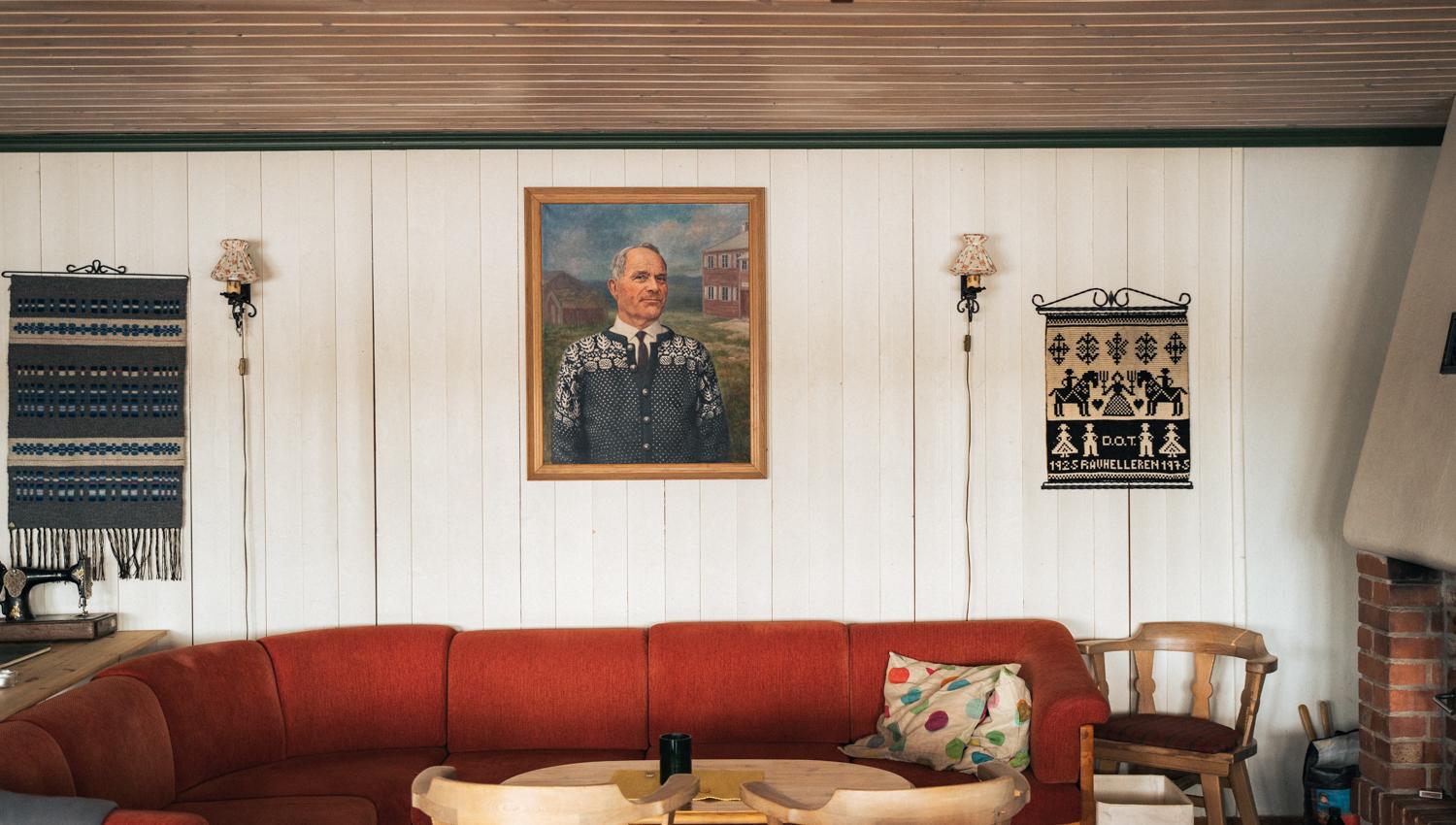 Inside the lodge, a lounge area with a red couch, wooden sitting chairs and a painting on the wall.