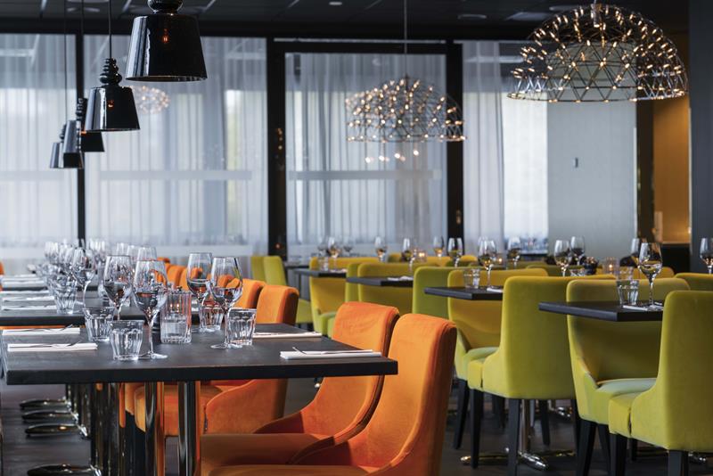 Restaurant med orange og grønne stoler og bord som er dekket på