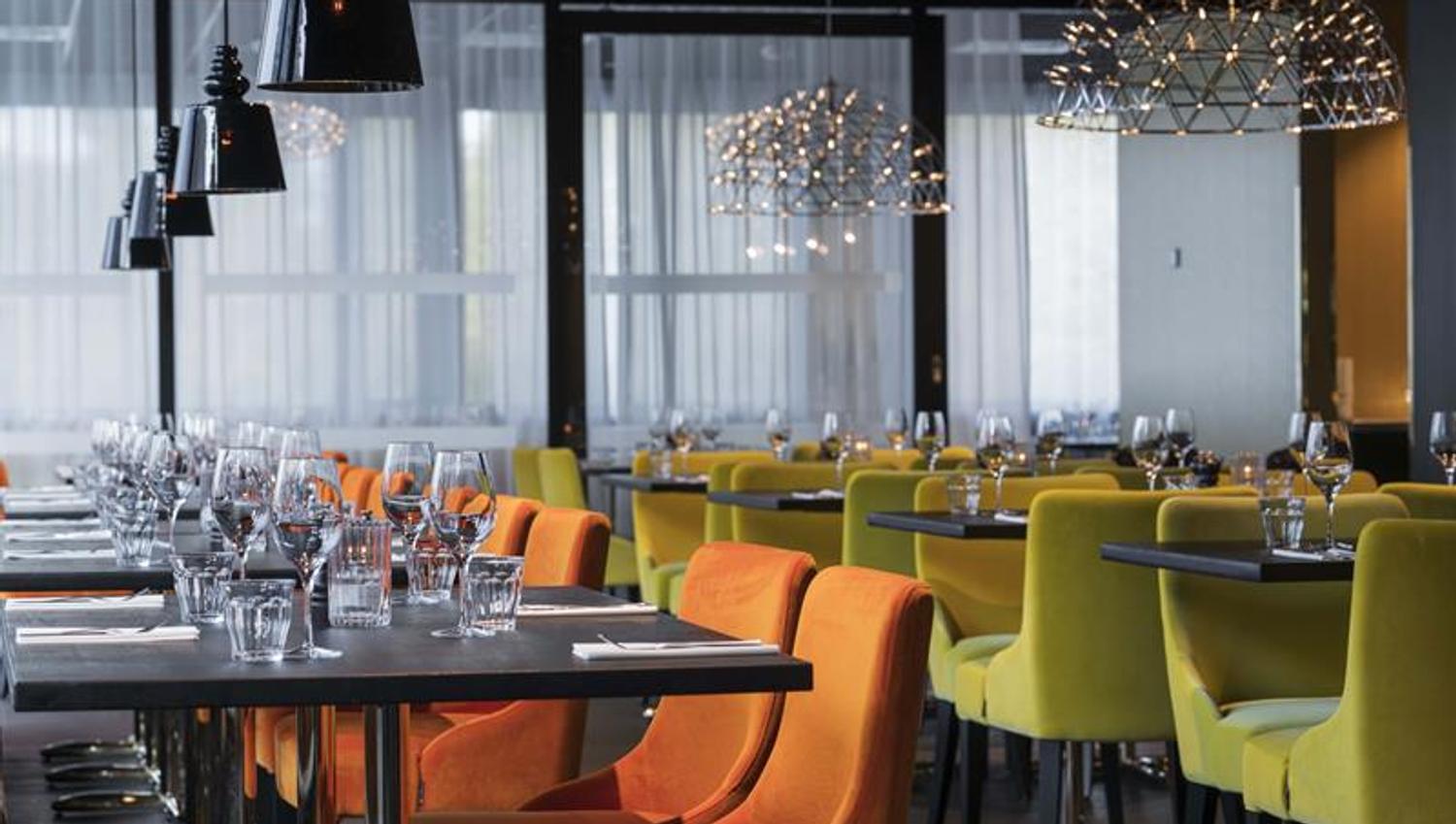 Restaurant med orange og grønne stoler og bord som er dekket på