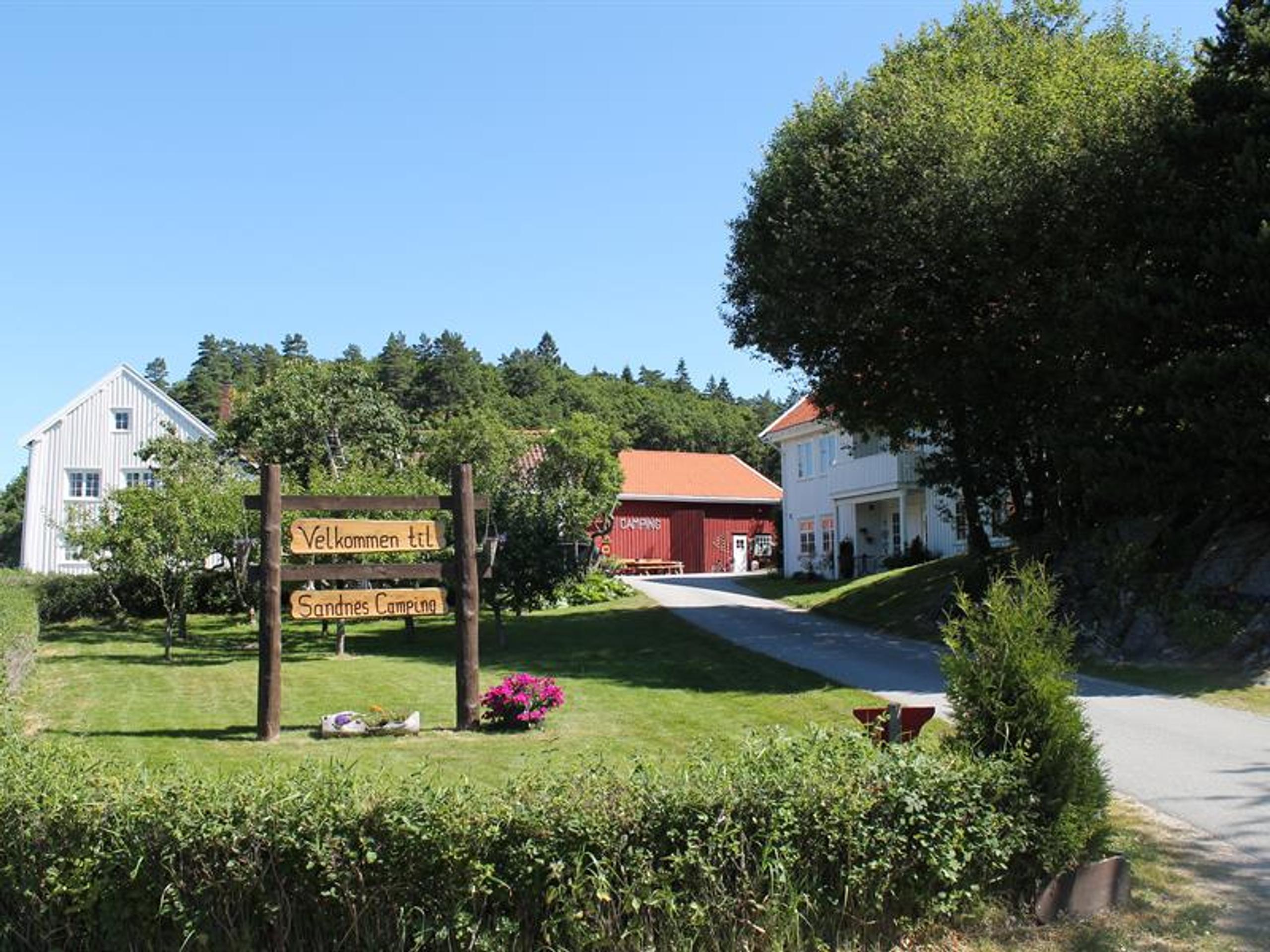 Entrance to Sandnes Camping. A large wooden sign reading "Welcome to Sandnes Camping" stands in a garden.