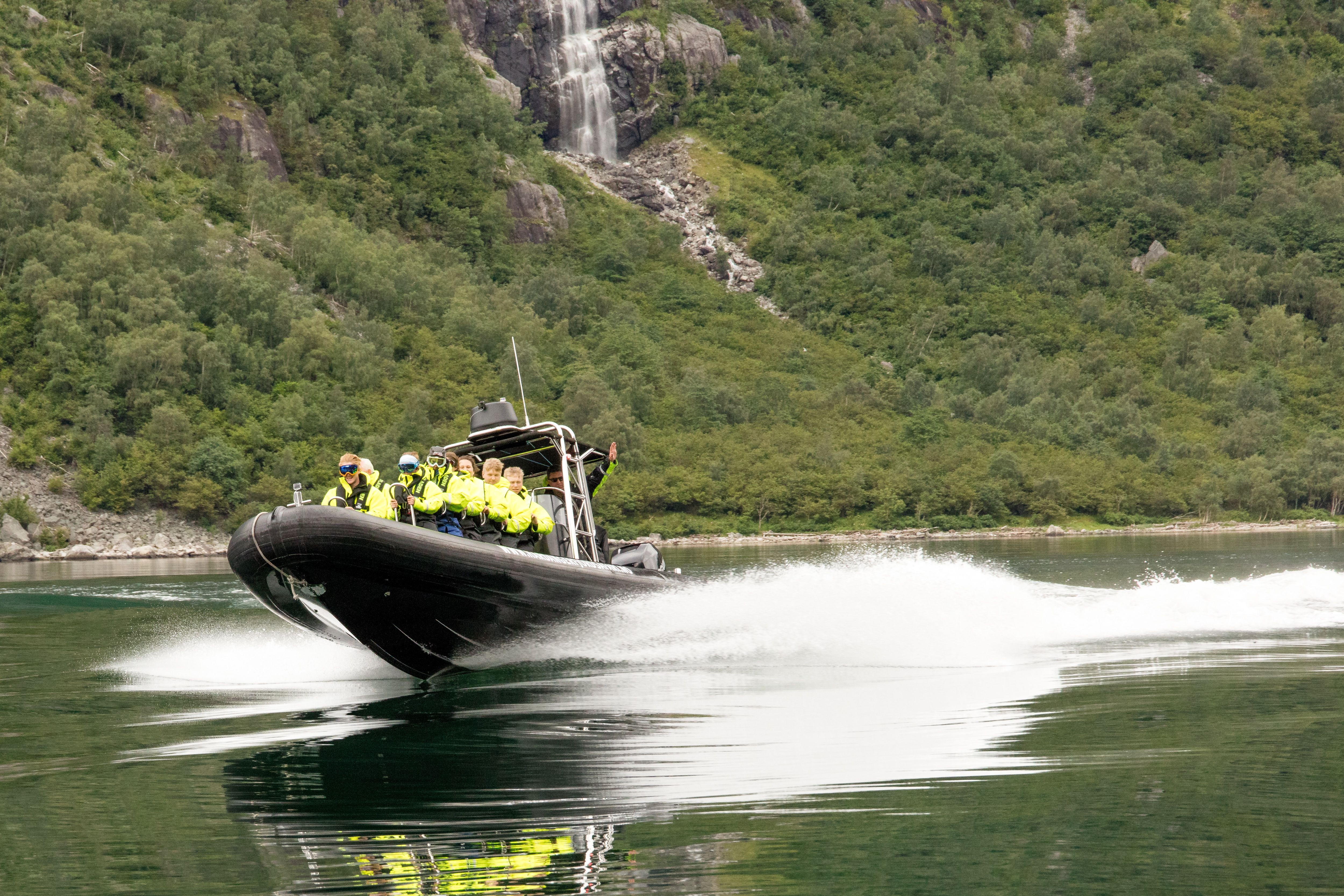 A rib boat filled with passengers speeding along on fjord.