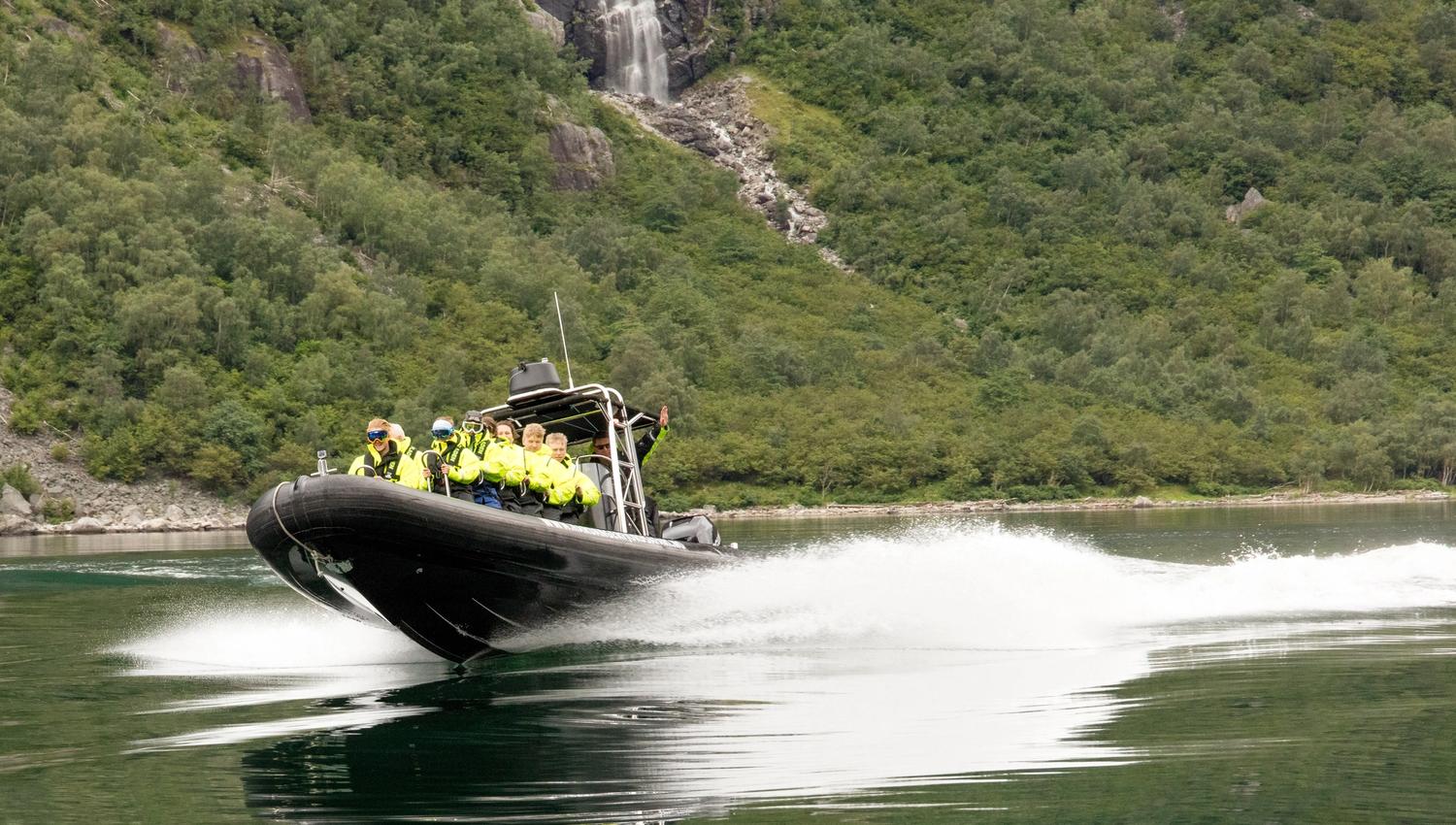 A rib boat filled with passengers speeding along on fjord.