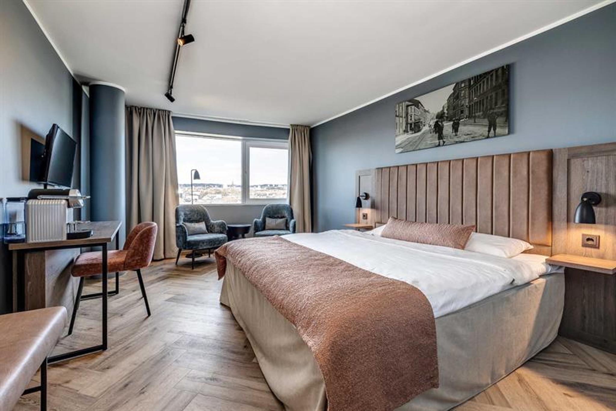 Hotellrom med dobbeltseng, skrivebord, to lenestoler og flott utsikt