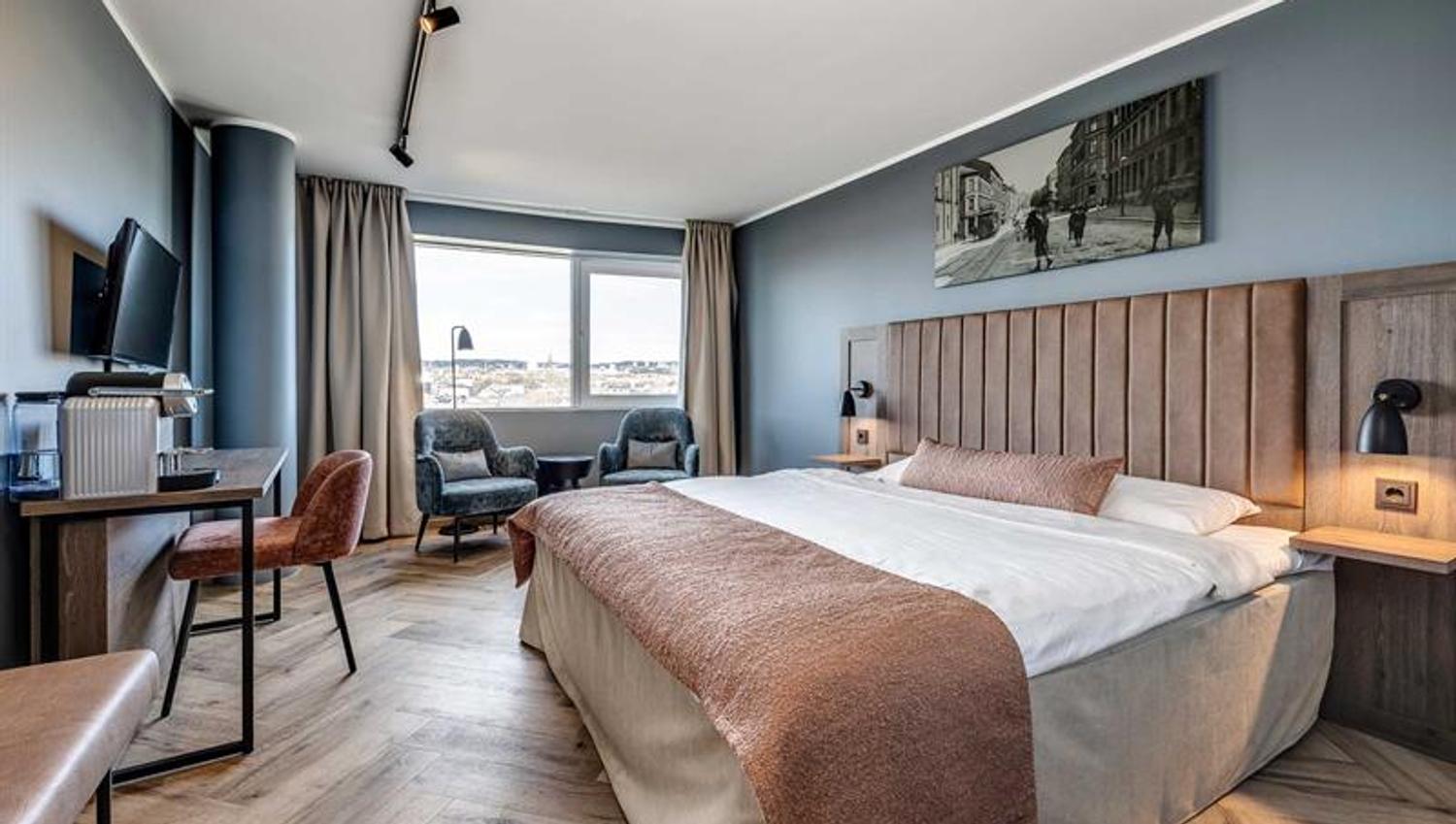 Hotellrom med dobbeltseng, skrivebord, to lenestoler og flott utsikt
