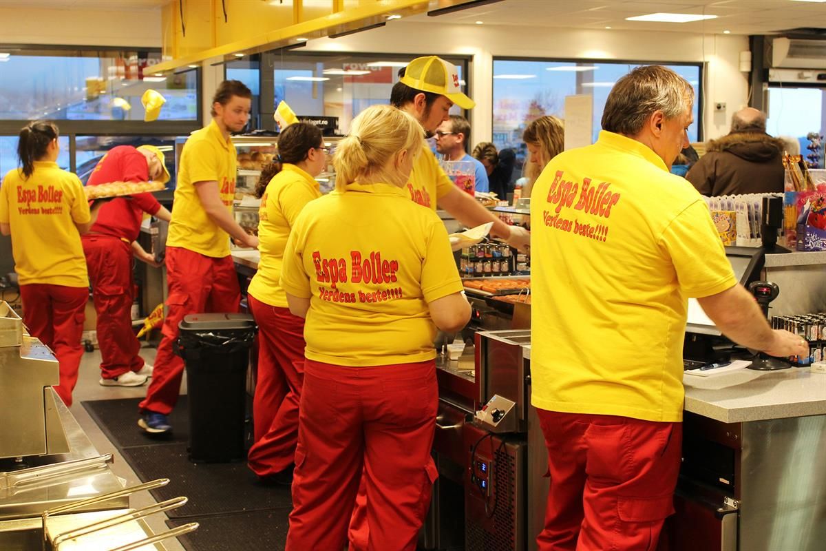 A group of employees wearing yellow and red uniforms working together behind the counter in a busy store or food service area.