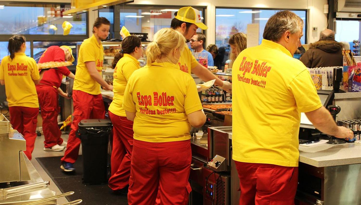A group of employees wearing yellow and red uniforms working together behind the counter in a busy store or food service area.