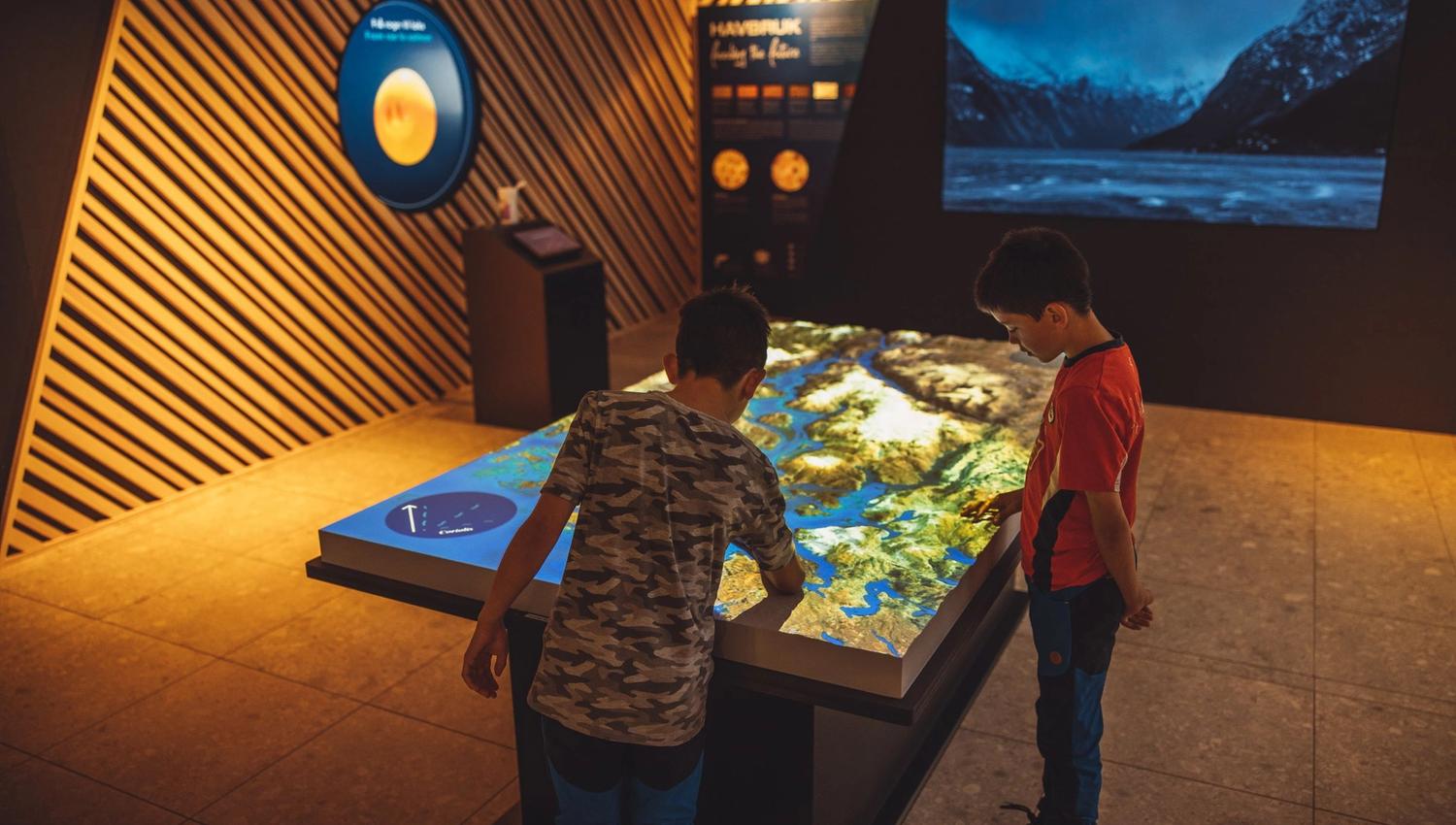 Children exploring the interactive landscape table in the “This is where we live” exhibition at the Hardanger Aquaculture Centre.