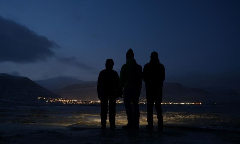 Three people looking towards Longyearbyen, and the blue light that colors the sky.