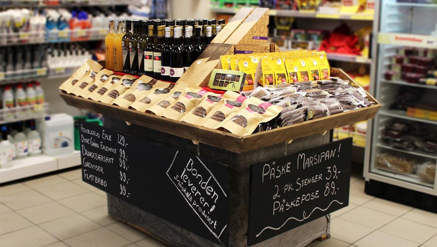 A store display island featuring an assortment of beverages and snacks, with handwritten chalkboard-style information on the sides.