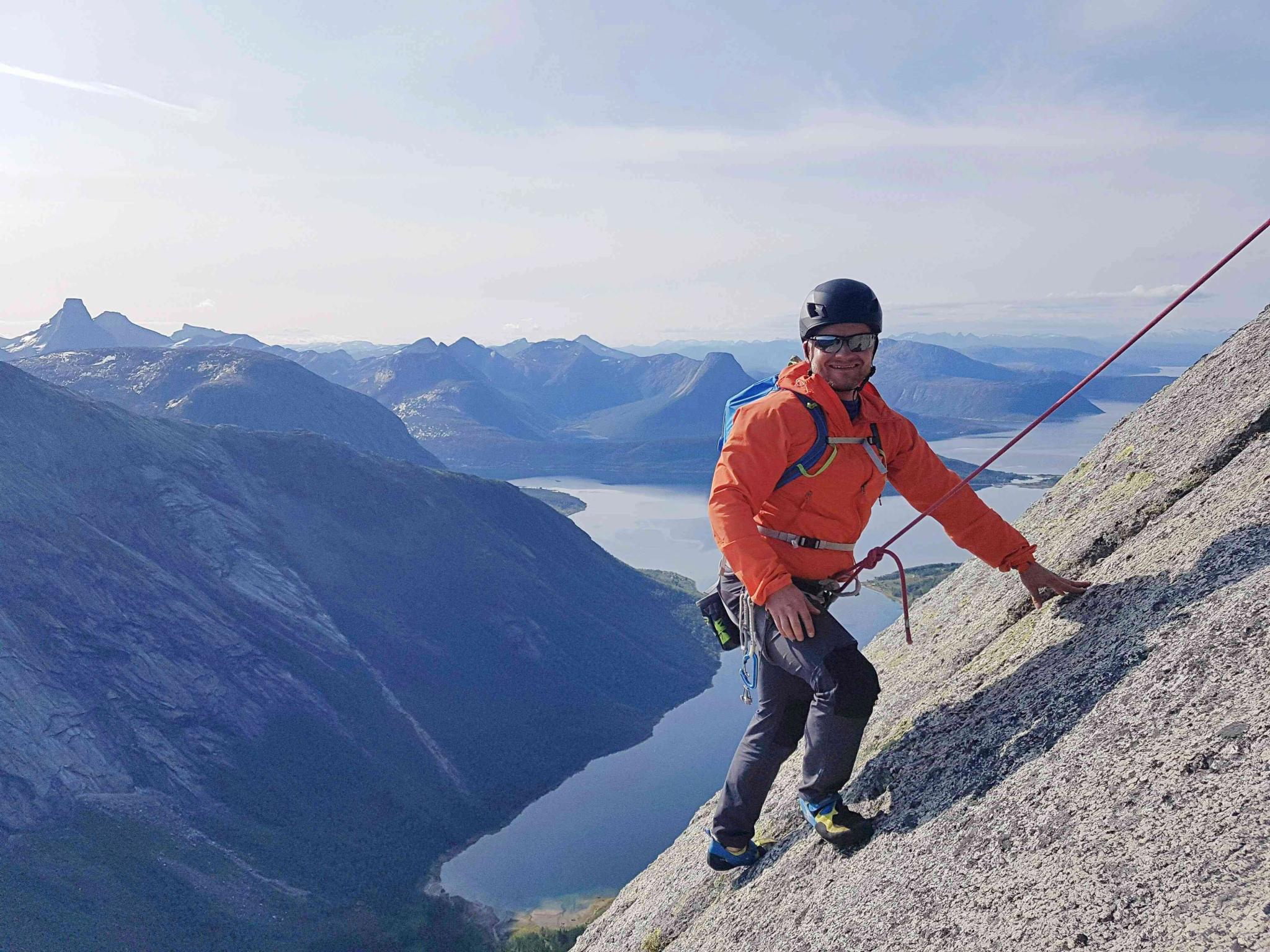 A man climbing up a mountainside with climbing gear on.